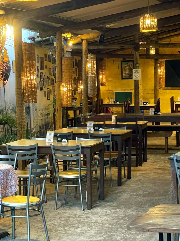 O salão do BhenzaDeus, com as mesas de madeira, as luminárias de palha acesas e a parede amarela