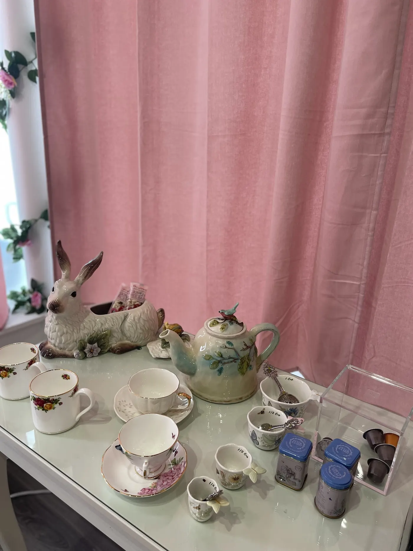A porcelain tea set and a rabbit figurine in front of a pink curtain at the studio