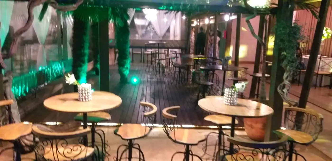 Deck à noite com mesas altas de madeira e luz verde nas plantas