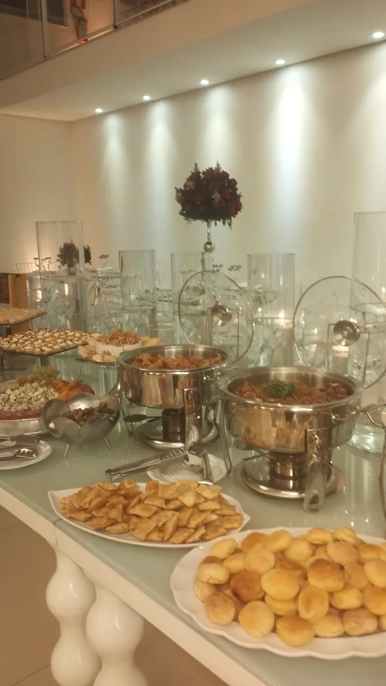 Mesa de salgados com réchauds e travessas num canto do salão