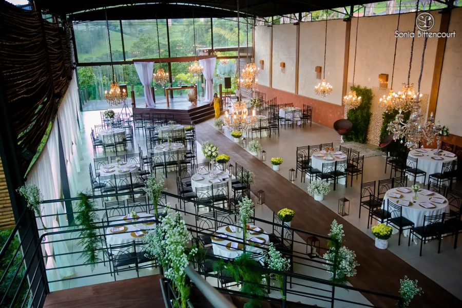Salão arrumado para casamento visto do alto, com lustres e mesas de toalha branca