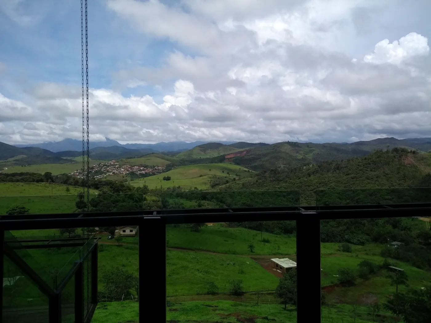 O vale verde visto do deck, com o guarda-corpo de vidro e a cidade ao longe