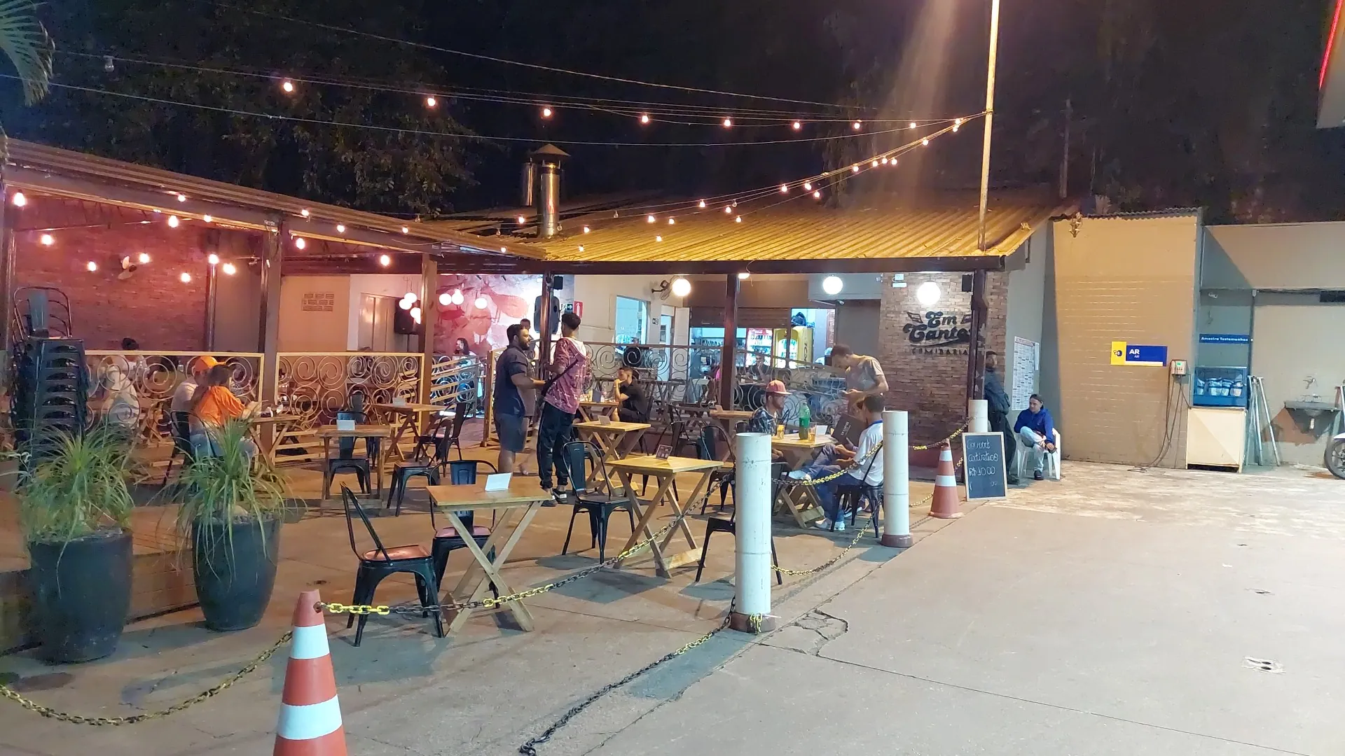 A área externa da Em Cantos à noite, com o varal de lâmpadas aceso sobre as mesas