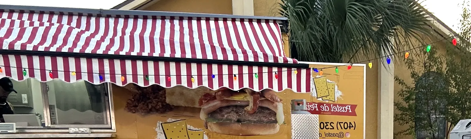 O truck amarelo com toldo listrado de vermelho e branco, um varal de luzinhas coloridas e o letreiro Pastel de Feira