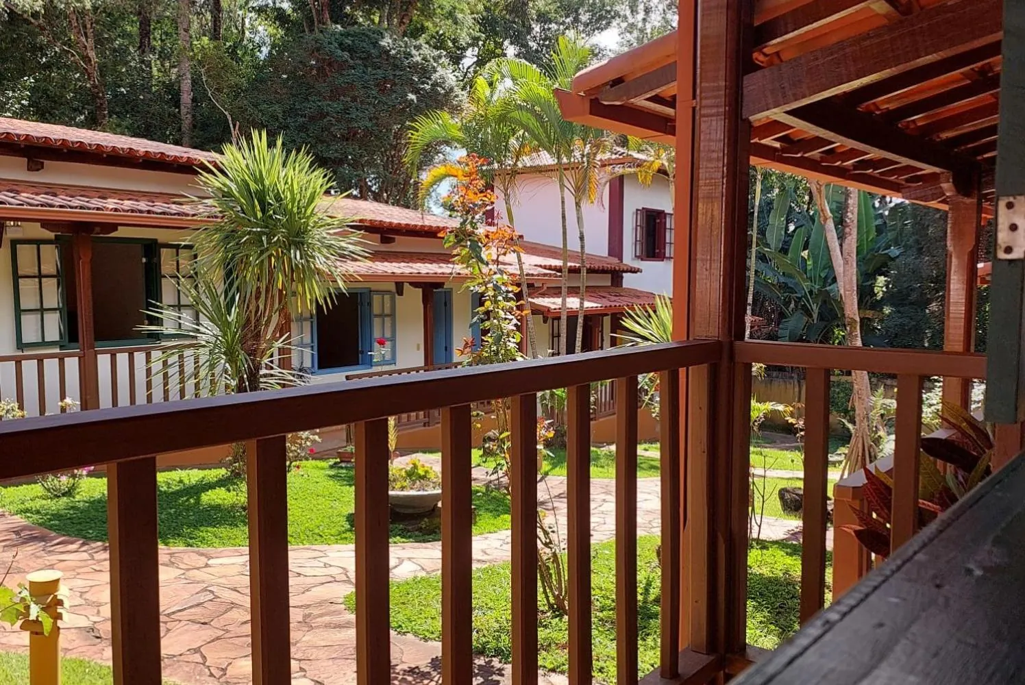 Vista da varanda de madeira para o jardim, com as palmeiras e as outras alas de quartos