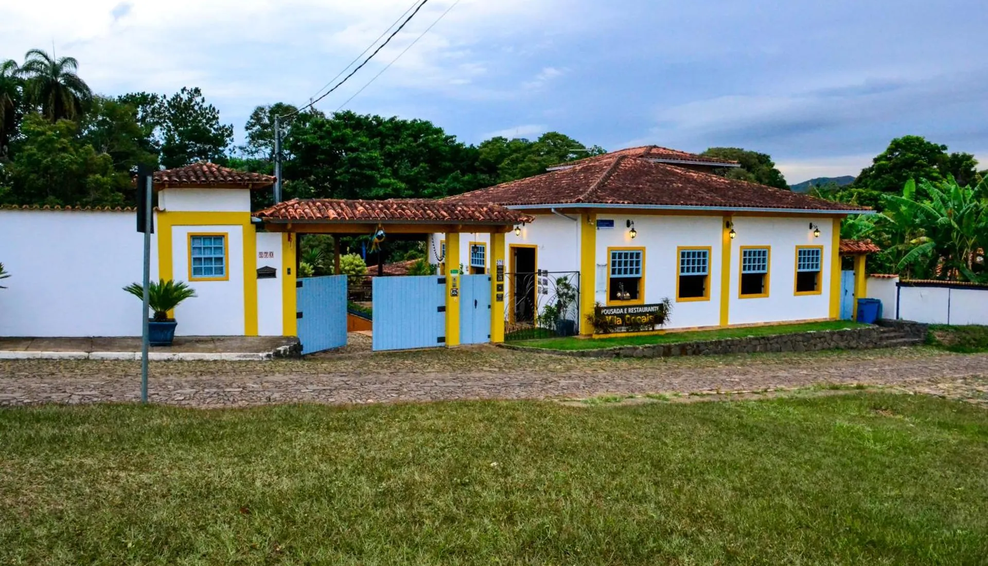 A fachada da pousada na rua de pedra, com as janelas azuis de moldura amarela