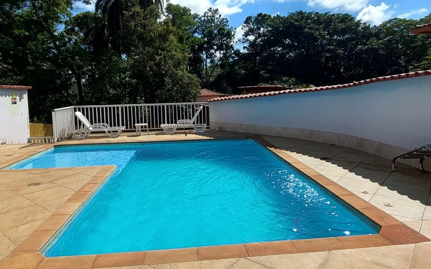 A piscina da pousada sob o céu azul, com o deque e as árvores em volta