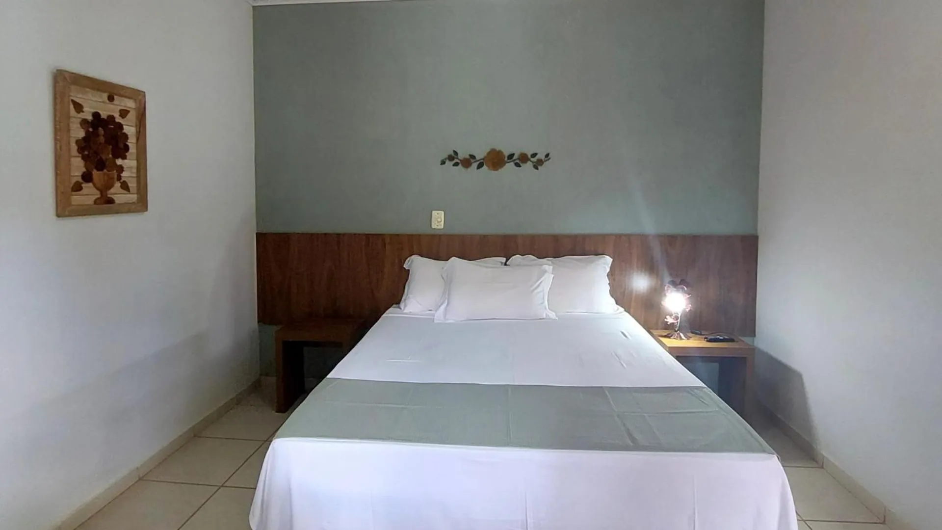 Quarto de casal da pousada, com parede verde-clara, cabeceira de madeira e ventilador de teto