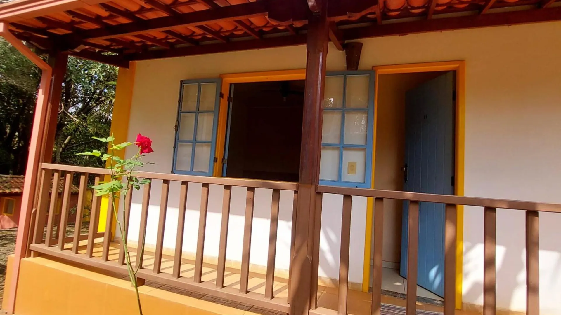 Varanda de madeira de uma suíte, com a porta azul e o jardim em frente