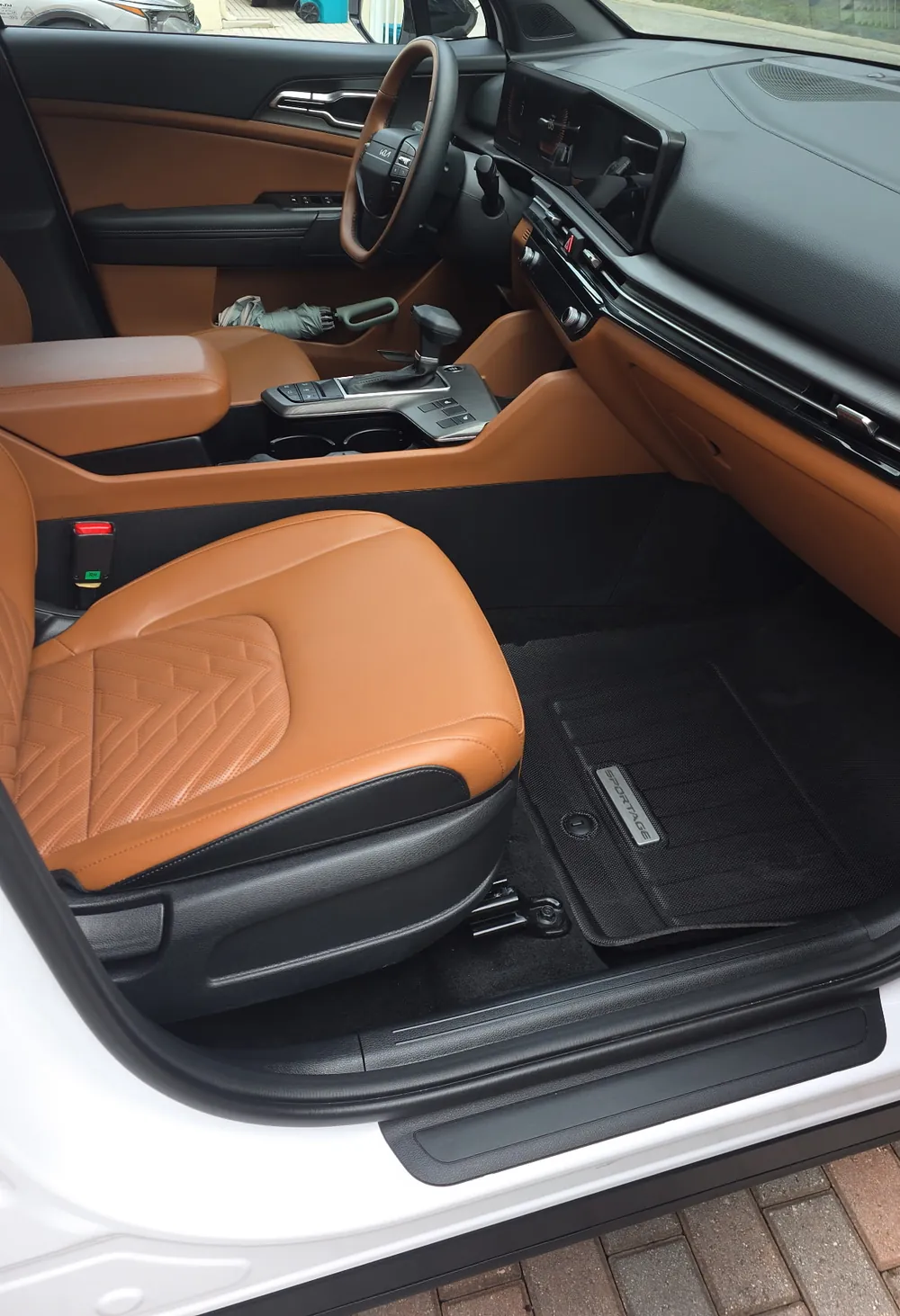 Clean tan leather front seats and floor mats of a white Kia, seen from the open driver door